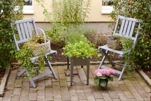 Zwei Klappstühle dekoriert mit Pflanzkörben darauf, ein kleiner Pflanztisch und ein Topf mit rosa Hortensien auf gepflastertem Boden
