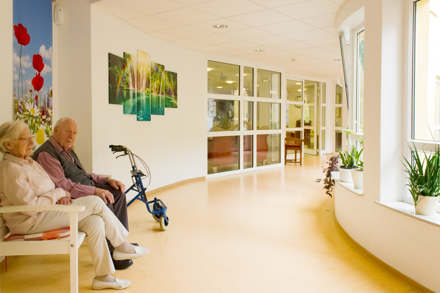 Zwei ältere Menschen sitzen auf einer Bank im hellen Flur